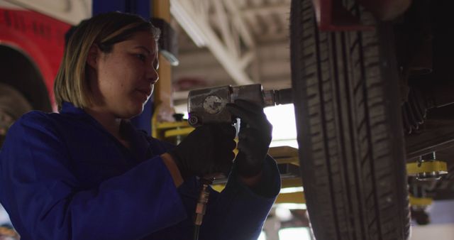 Female mechanic changing tires of the car using a power drill at a car service station. automobile repair service