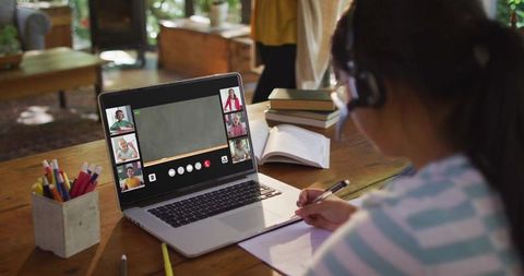 Girl Studying Remotely Writing Notes While Attending Virtual Class on Laptop with Headset