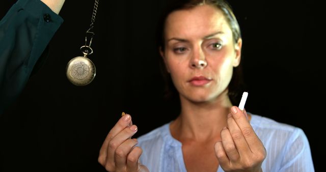 A Caucasian woman appears focused on a broken cigarette while a hypnotist's pendulum swings in the foreground, suggesting a session aimed at quitting smoking. Hypnotherapy is often sought as a method to overcome addictions and change behaviors.