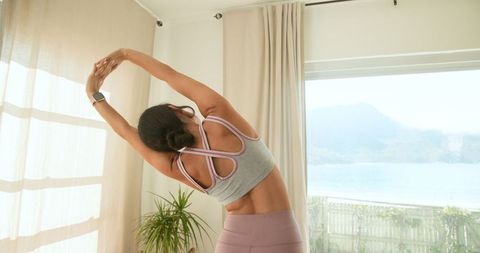 Woman Practicing Side Stretch by Glass Panel in Bright Room