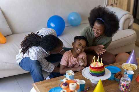 Happy african american family celebrating child birthday with rainbow cake and balloons