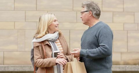 Senior couple chatting while holding coffee cups and shopping bags on urban street