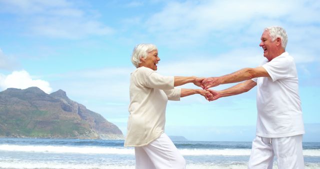 A senior Caucasian couple is holding hands and smiling at each other on a sunny beach, with copy space. Their joyful expression and casual attire suggest a moment of leisure and happiness during retirement.