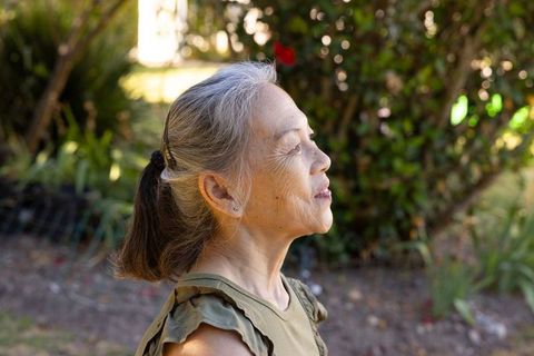Senior asian woman enjoying sunlight in backyard, eyes closed, profile, peaceful mindfulness