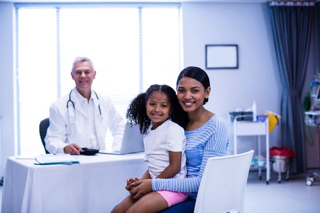 Mother and daughter visiting doctor in clinic. Doctor sitting at desk with laptop, smiling. Mother and daughter sitting on chair, smiling. Suitable for healthcare, family health, medical consultation, pediatric care, and hospital-related content.
