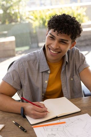 Young creative man smiling while writing in calm outdoor setting