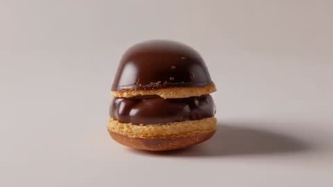 Rotating camera revealing glossy chocolate eclair on beige tabletop showing glaze and layers