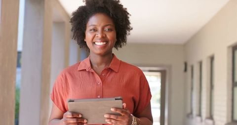 Smiling african woman in her 30s holding tablet in corridor for business and education