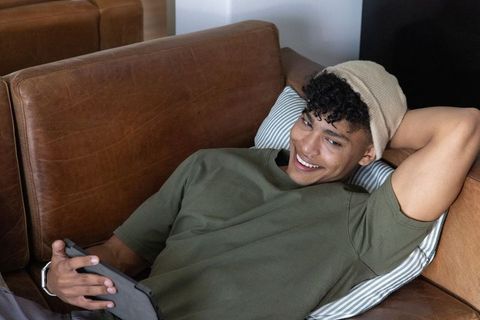 Smiling african american man relaxing on leather sofa with tablet, casual home lifestyle