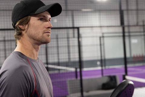 Focused padel player wearing cap watching match on indoor purple court holding racket