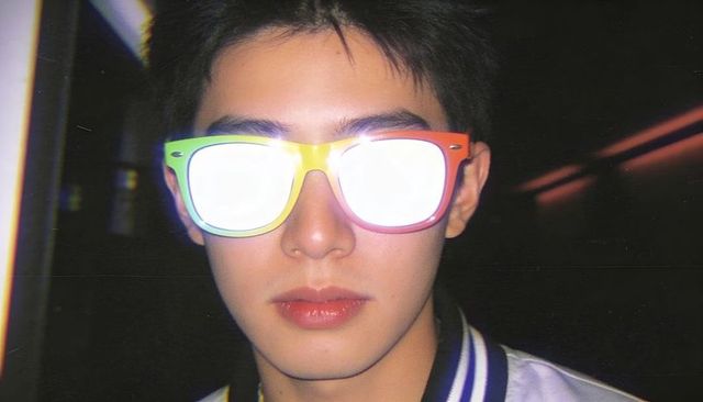 Young man wearing rainbow sunglasses reflecting flash in neon low-light portrait