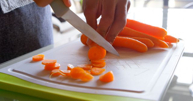 A person is slicing carrots on a white cutting board, with copy space. Careful knife skills are demonstrated in the preparation of fresh vegetables for a healthy meal.