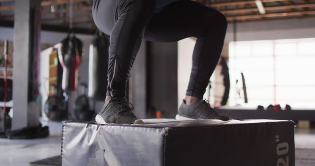 Person performing a box jump exercise in a gym environment, focusing on their legs. Useful for illustrating topics related to fitness, training routines, and athletic performance. Ideal for health and fitness blogs, workout programs, gym promotional materials, and sports-related articles.