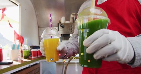 Street vendor serving fresh orange and green juices in disposable cups wearing gloves