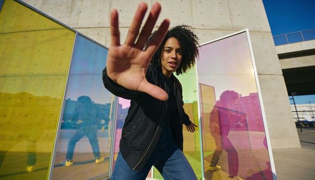 Dynamic young woman reaching toward camera with iridescent panels and urban reflections