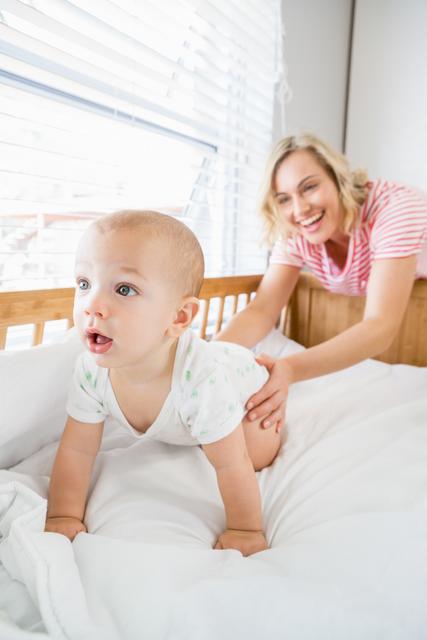 Mother interacting with her baby boy in a crib at home. Ideal for themes related to parenting, family bonding, child care, and early childhood development. Perfect for blogs, websites, or advertisements focused on family life, parenting tips, and children's products.