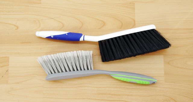 A pair of brooms laying on a wooden floor, one with black bristles and another with white bristles. This image is suitable for illustrating concepts of domestic cleaning, household maintenance, or hygienic practices. It can be used in articles or advertisements related to cleaning services, home care routines, or cleaning products.