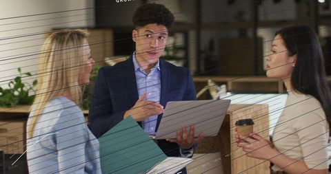 Young professional presenting laptop at coworking counter while team discussing project