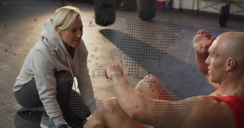 Female Trainer Coaching Male Athlete Doing Sit-ups on Rubber Gym Floor During Workout
