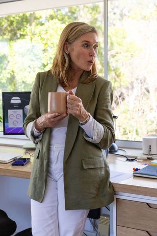 Mature businesswoman holding mug by workstation in modern office