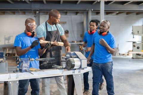 African american instructor teaching apprentices woodturning on lathe in woodworking shop