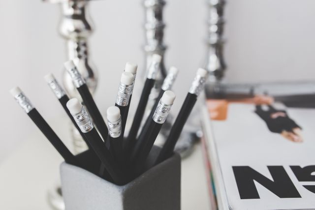 A bundle of black pencils with white erasers neatly placed in a pencil holder on a desk. The scene includes a close-up view of the stationery, implying organization and readiness for writing tasks. Suitable for use in blogs about office organization, educational settings, productivity, and workspace setup.