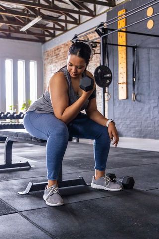 Asian woman performing seated dumbbell curl in industrial gym, strength training daylight