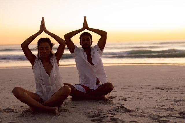 Couple performing yoga together on the beach - Download Free Stock Photos Pikwizard.com