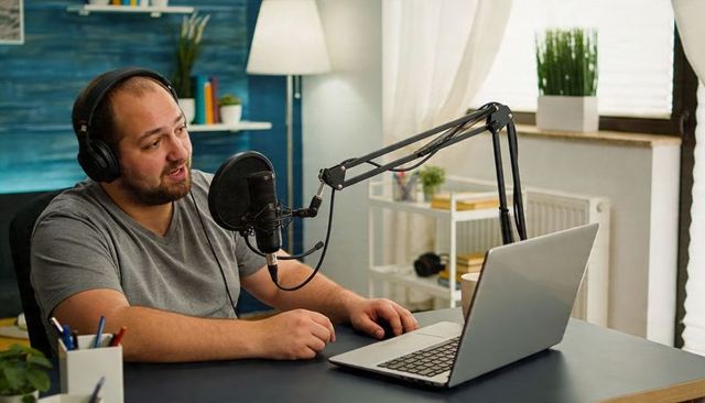 Bearded man recording podcast in home studio, wearing headphones and using laptop