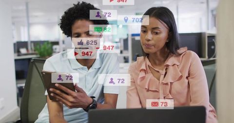 Coworkers analyzing social media metrics on tablet and laptop in modern open office