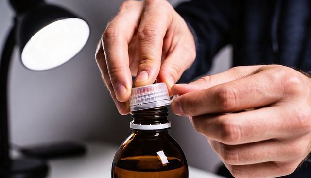 Hands removing tamper-proof seal from amber medicine bottle close-up