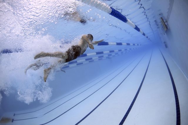 Swimmers captured underwater competing in a race, performing freestyle stroke in a swimming pool. Splashing water and motion blur emphasize action and intensity. Great for usage in sports articles, fitness and training blogs, swim school promotions, or motivational content focused on competitive sports.