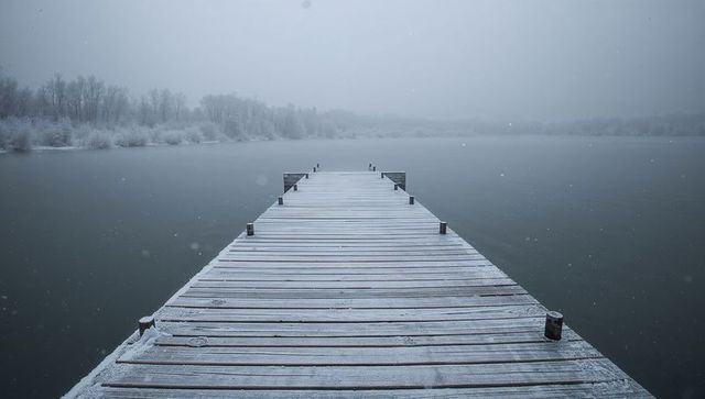 Snow-dusted wooden pier leading into misty winter lake horizon, serene dock perspective