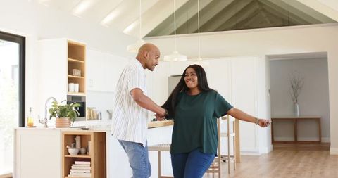 African american couple holding hands and dancing in modern open-plan kitchen