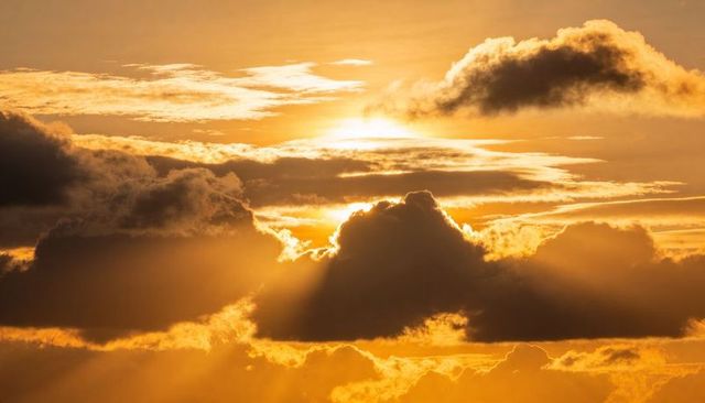 Golden sunrise glowing behind cumulus cloud casting crepuscular rays and dramatic rim light