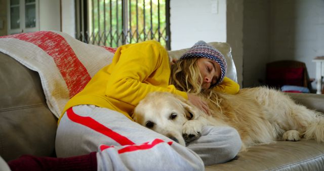 Happy caucasian female teenager wearing cap sleeping with her dog at home. Domestic life, pets, animals and care, unaltered.
