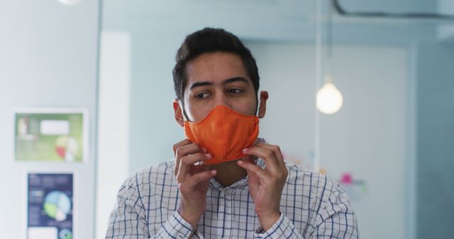 Young Man Adjusting Orange Face Mask in Office Setting - Download Free Stock Images Pikwizard.com