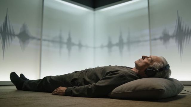 Senior man relaxing with headphones listening to waveform on backlit minimalist panel