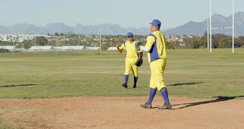 Baseball players walking on field wearing yellow and blue uniforms with mountain backdrop
