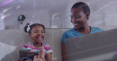 Mother and daughter laughing on sofa using tablet and laptop with ar overlay