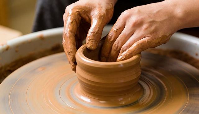Hands shaping clay on spinning pottery wheel crafting handmade ceramic pot in studio