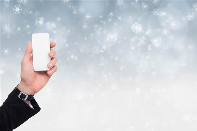 Digital composite of Cropped image of hand holding smart phone with snowflakes in background