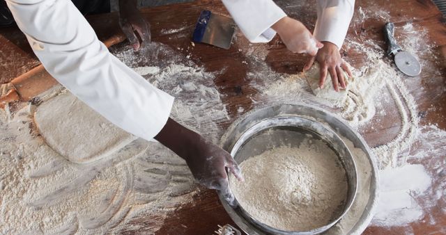 Hands of chefs rolling and kneading dough on floured surface in a professional kitchen. Ideal for content related to culinary arts, baking, cooking classes, hospitality industry, teamwork, and food preparation. Great for illustrating teamwork and the process of making bread, pastries, or other baked goods.