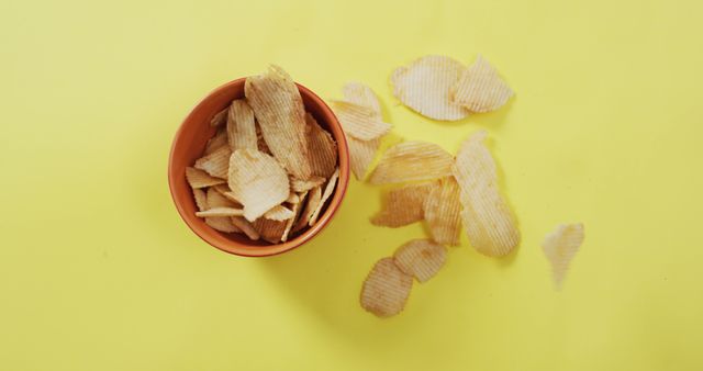 Close up of potato chips falling in a bowl on yellow surface. food and snack concept