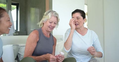 Multiethnic mature women discussing medication and health while sitting on living room sofa