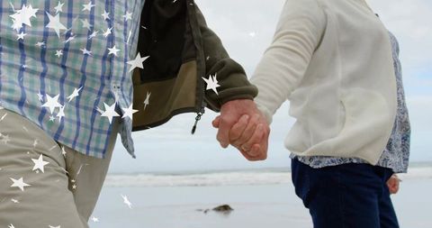 Senior couple holding hands on beach strolling peaceful coastline