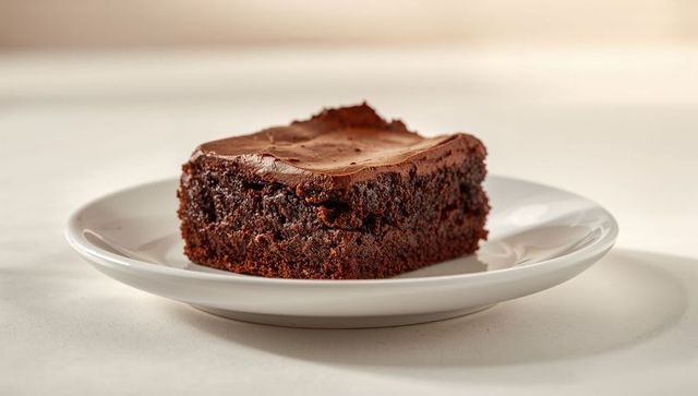 Presenting frosted chocolate brownie on white plate close-up with moist fudgy texture