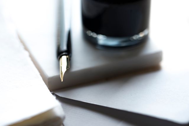 Fountain pen resting near ink bottle on a stack of white papers; perfect for highlighting stationery products, writing habits, or scenes of professional work. Ideal for illustrating creative writing concepts, office or study environments.