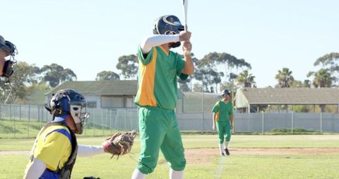 Batter Preparing to Swing in Green and Yellow Uniforms with Catcher on Sunny Baseball Field