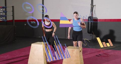 Two women performing box jumps with fitness data overlays in boxing gym